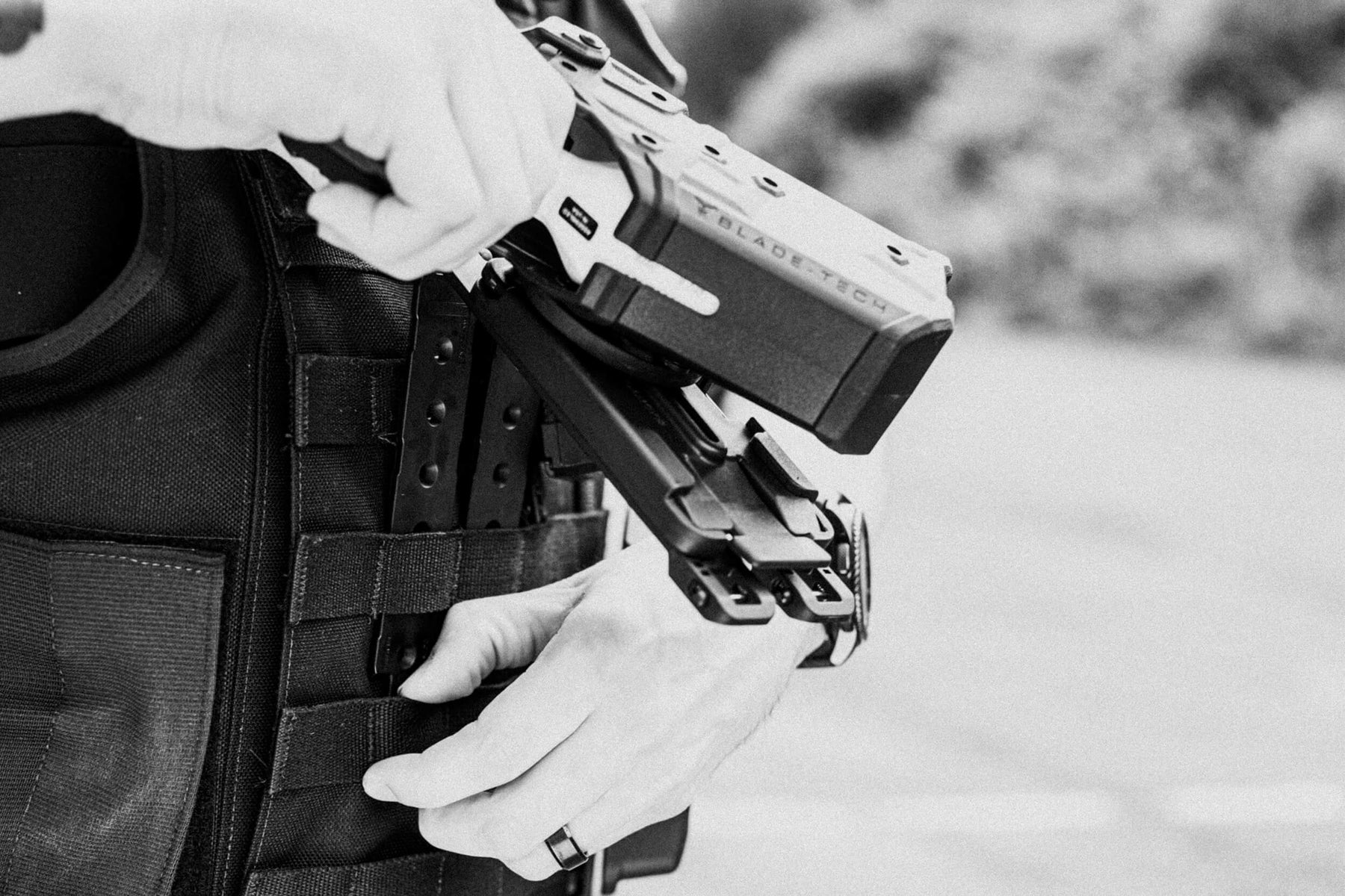 Person attaching Molle-Lok Attachment onto Molle-Webbing Duty Vest with TASER Outside the Waistband (OWB) Holster with Large TMMS (Tactical Modular Mount System)